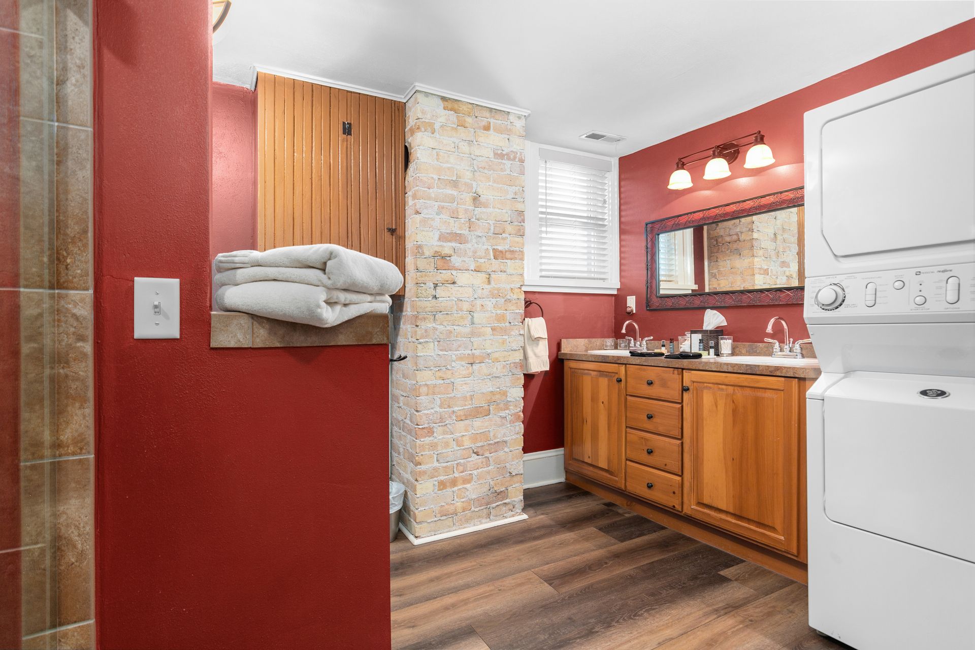 Bathroom with red walls, wooden vanity, stacked washer/dryer, stone accent wall, and stacked white towels.