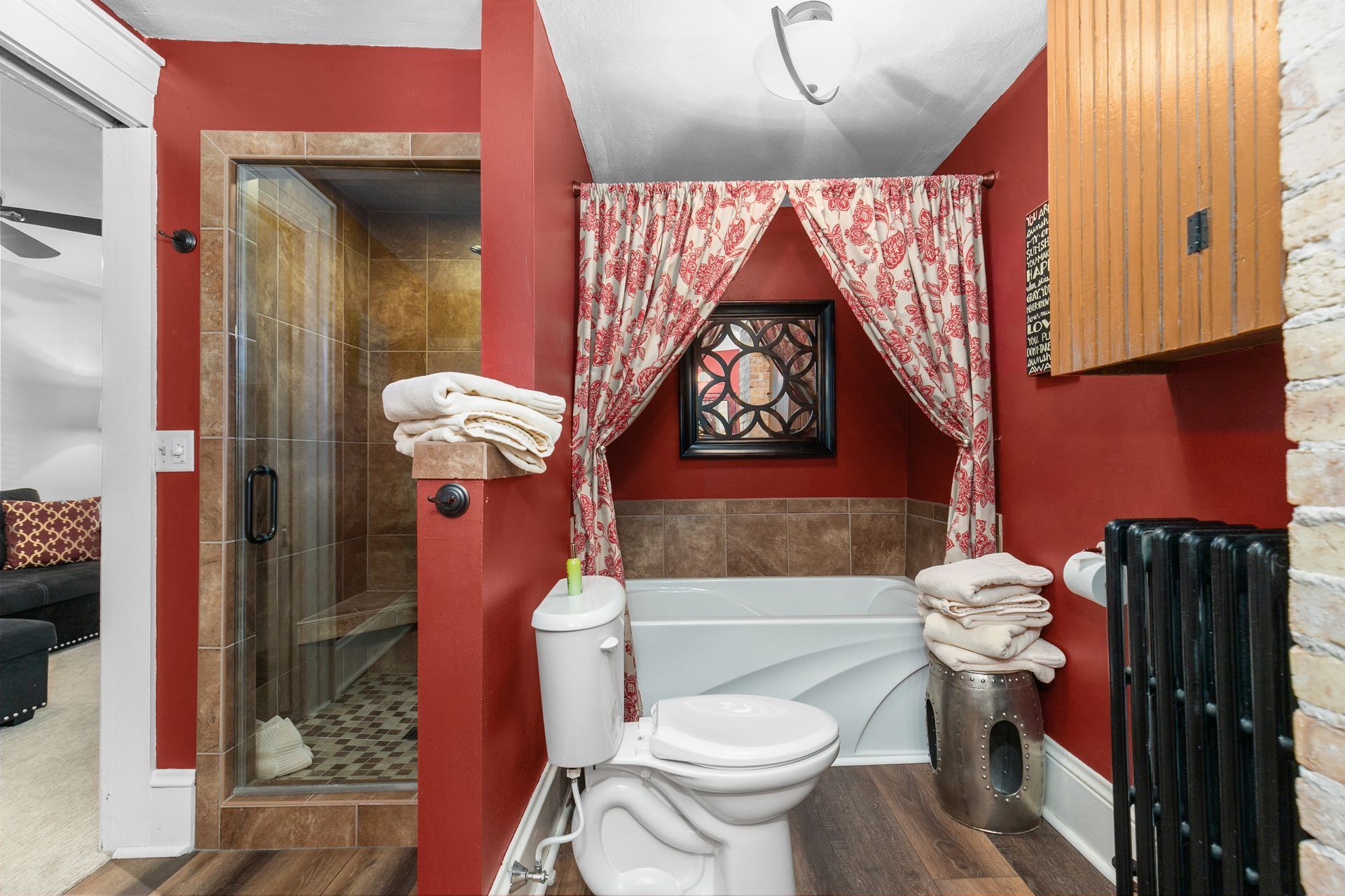 Red bathroom with a shower, toilet, and bathtub under a patterned curtain.