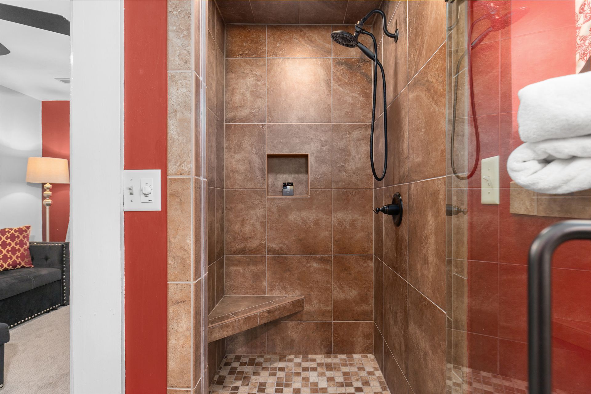 A brown tiled shower with a bench seat, glass door, and a stack of white towels.