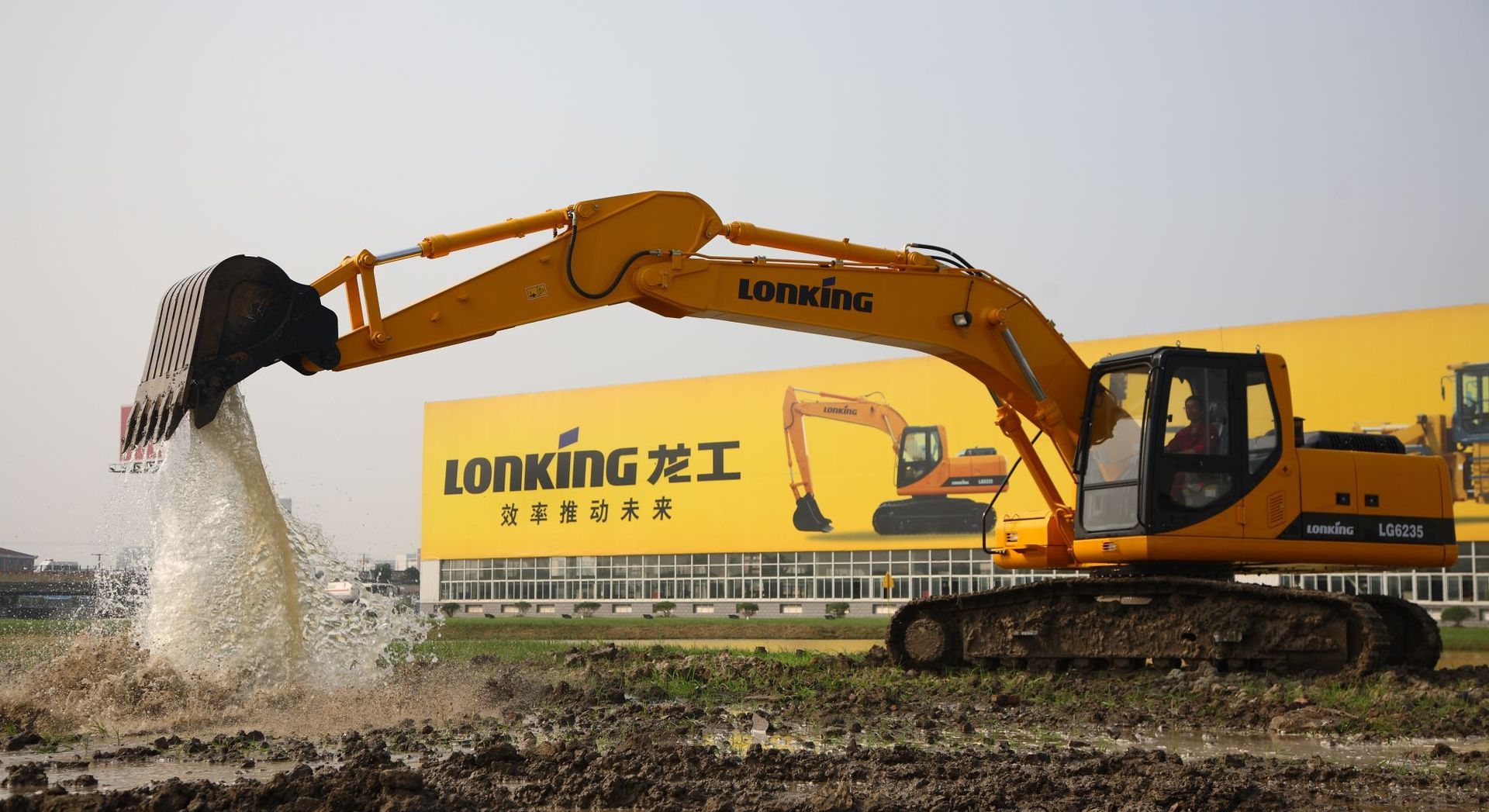 Yellow excavator spraying water into a muddy field near a Lonking sign.