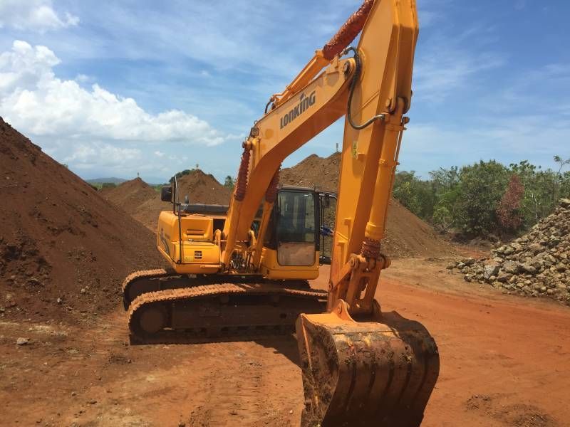 Yellow excavator on a dirt road in front of a brown dirt pile, under a cloudy sky.
