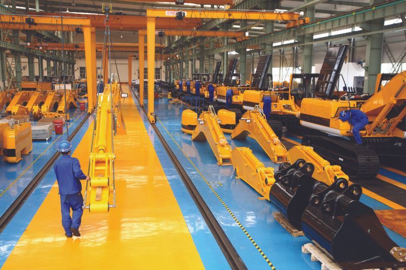 Workers in a large factory assembling yellow and black construction equipment.