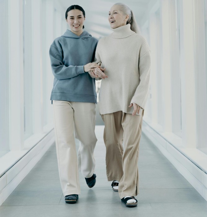 Two people walking hand in hand through a bright corridor, smiling and wearing light-colored clothing.