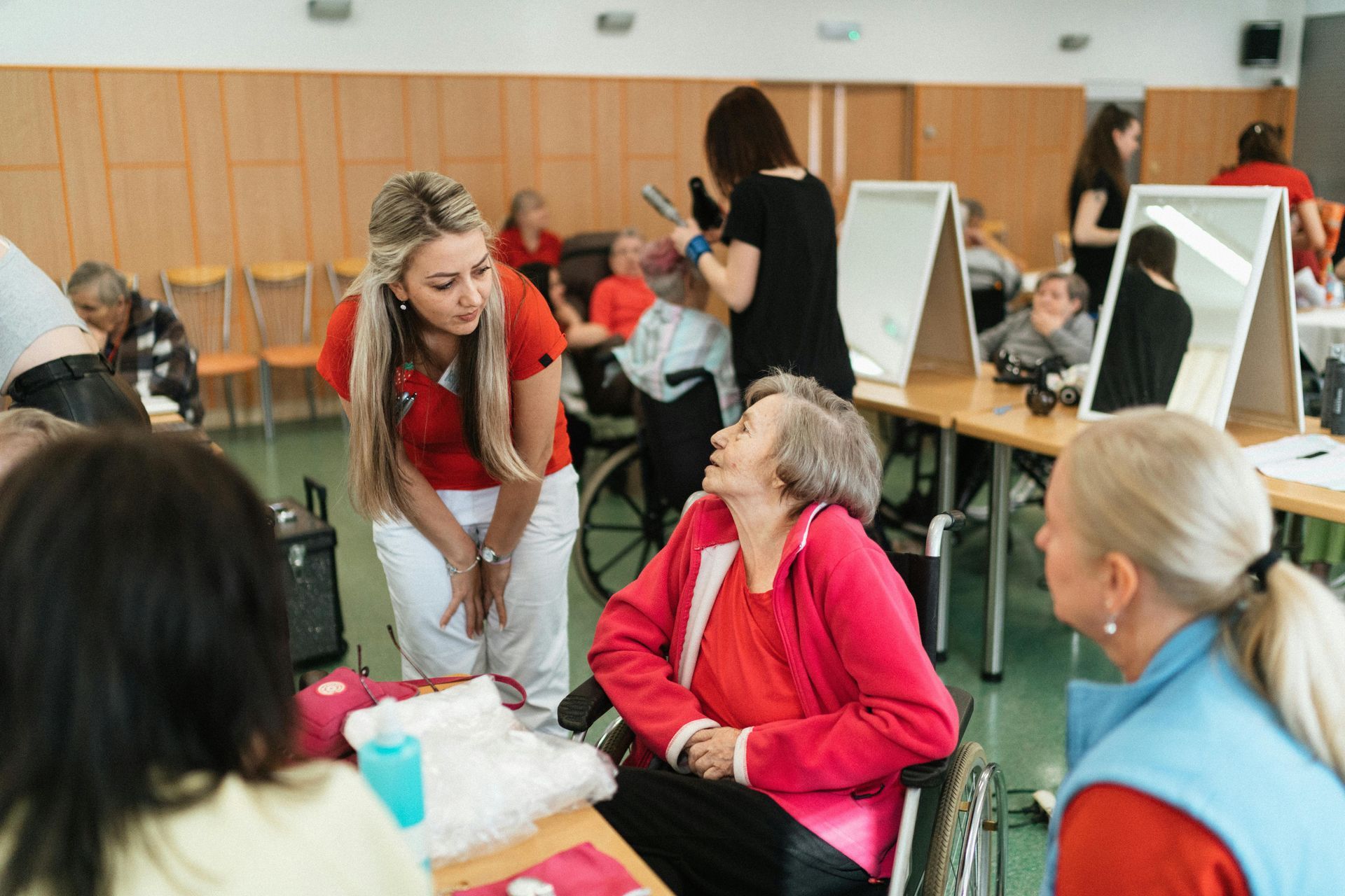 Woman in a red vest talks with an older woman at a table in a busy indoor event hall.
