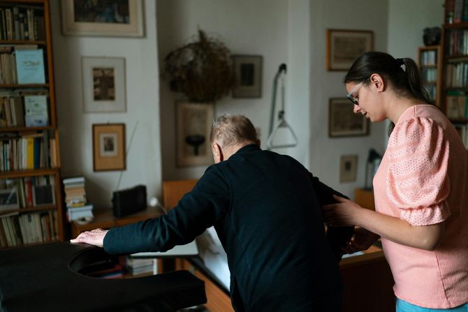 Two people working at a piano in a framed, book-lined living room