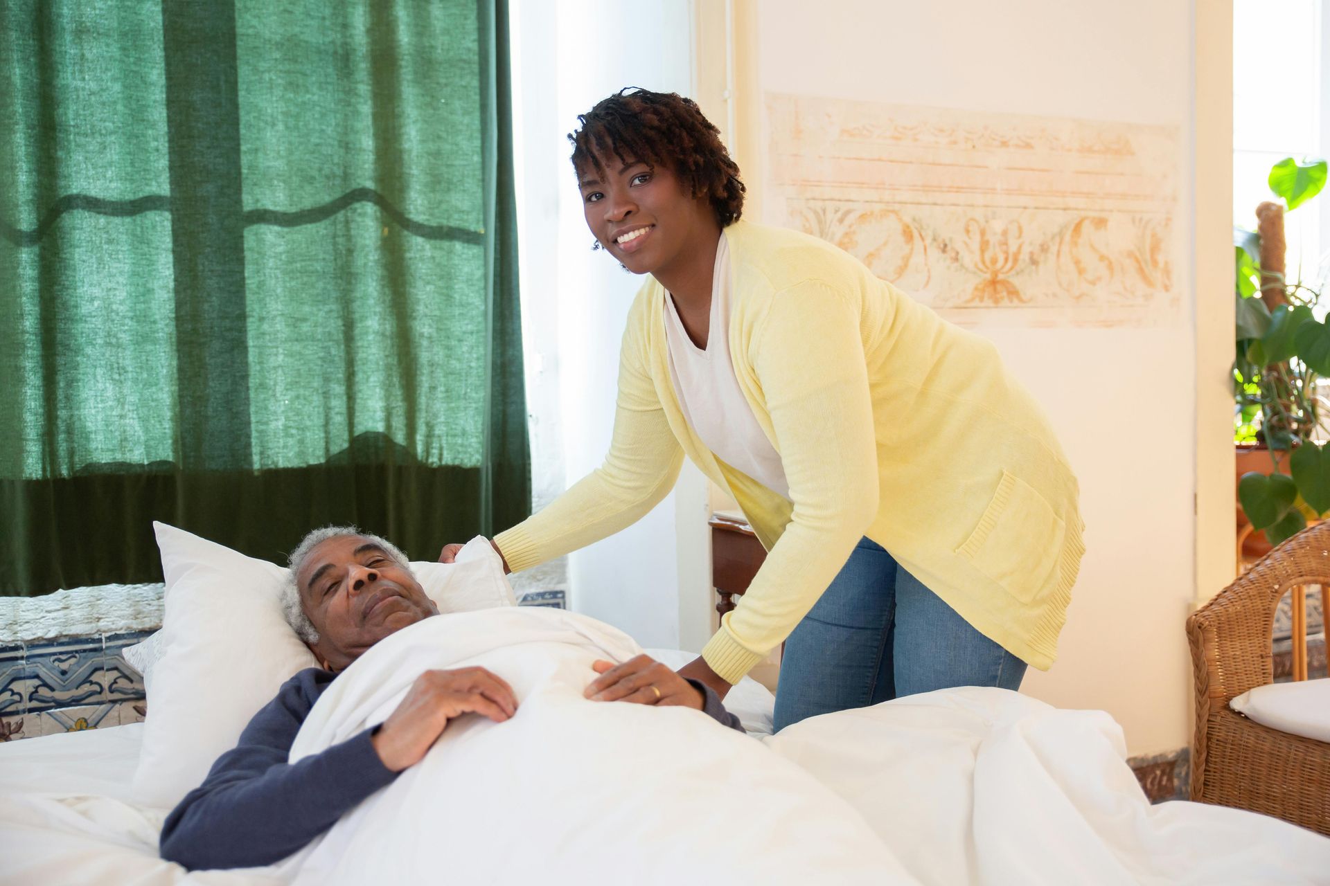 Woman leaning over a man in bed, smiling in a bright room with green curtains.