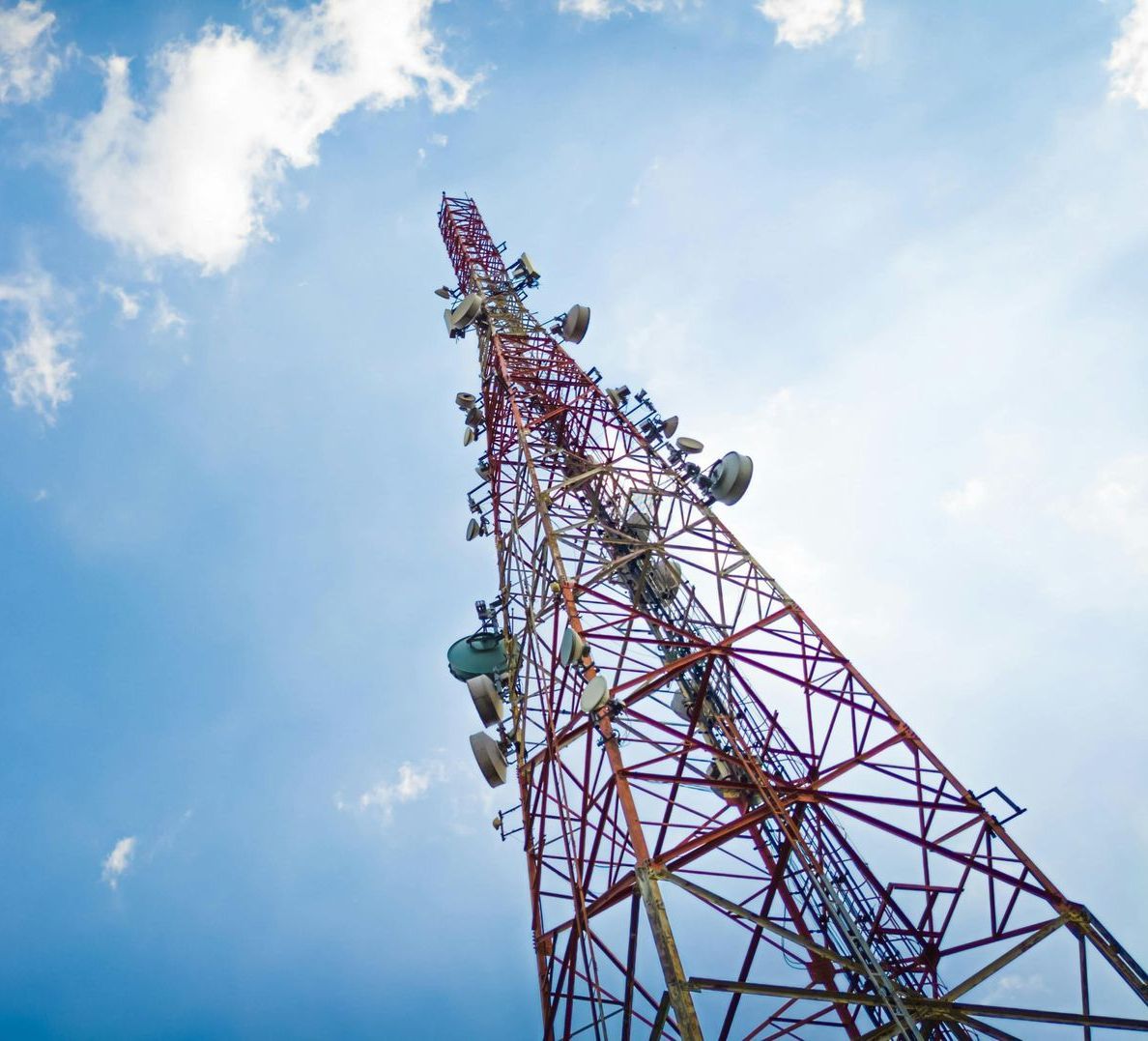 A red and white telephone tower against a blue sky with clouds.