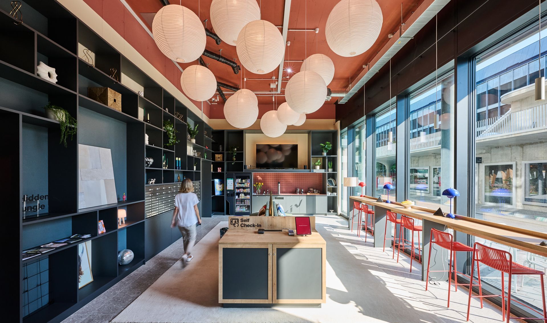 A woman is walking through a room with a lot of windows and lanterns hanging from the ceiling.
