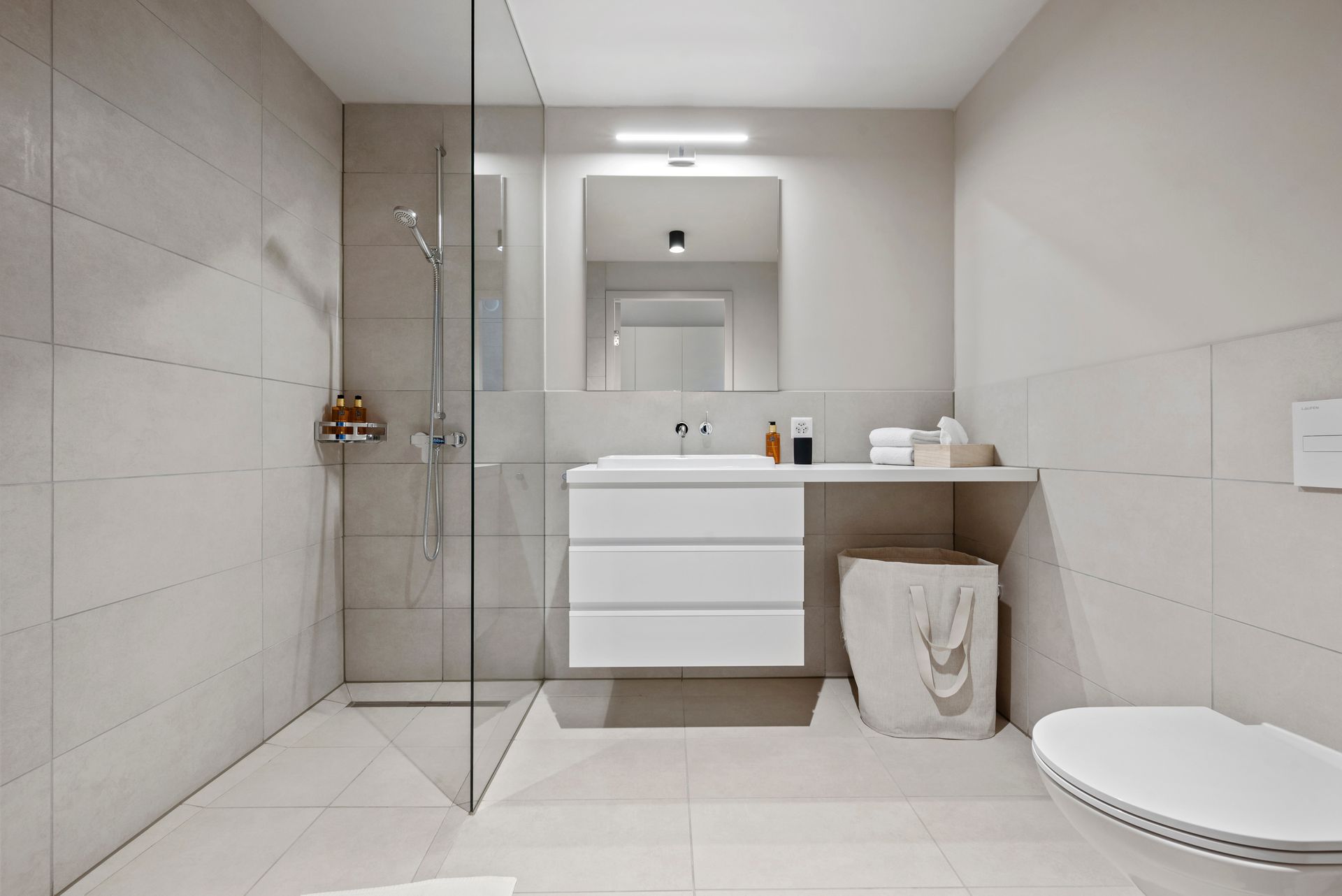 Ein Badezimmer mit ebenerdiger Dusche, Waschbecken, Toilette und Spiegel.