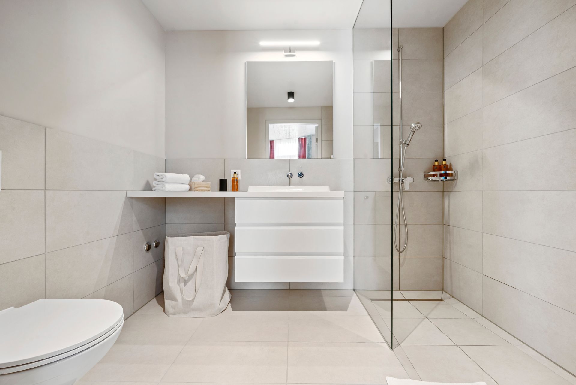 Ein Badezimmer mit Toilette, Waschbecken, Spiegel und ebenerdiger Dusche.