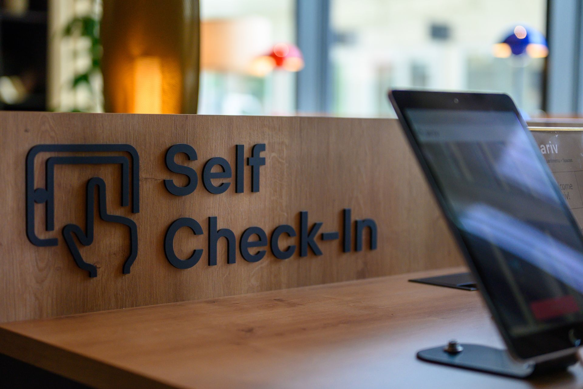 A tablet is sitting on a wooden table next to a sign that says self check-in.