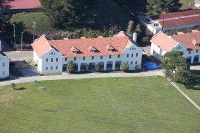 White building with orange tile roof, three dormers, and arched porch; set on a grassy field.
