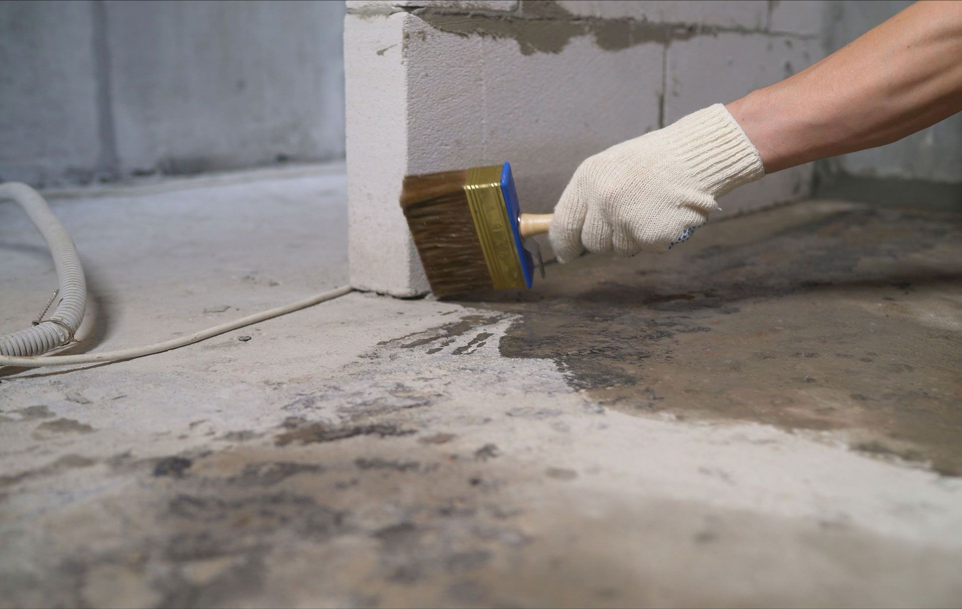 Construction worker applying waterproofing coating on concrete floor for moisture protection.