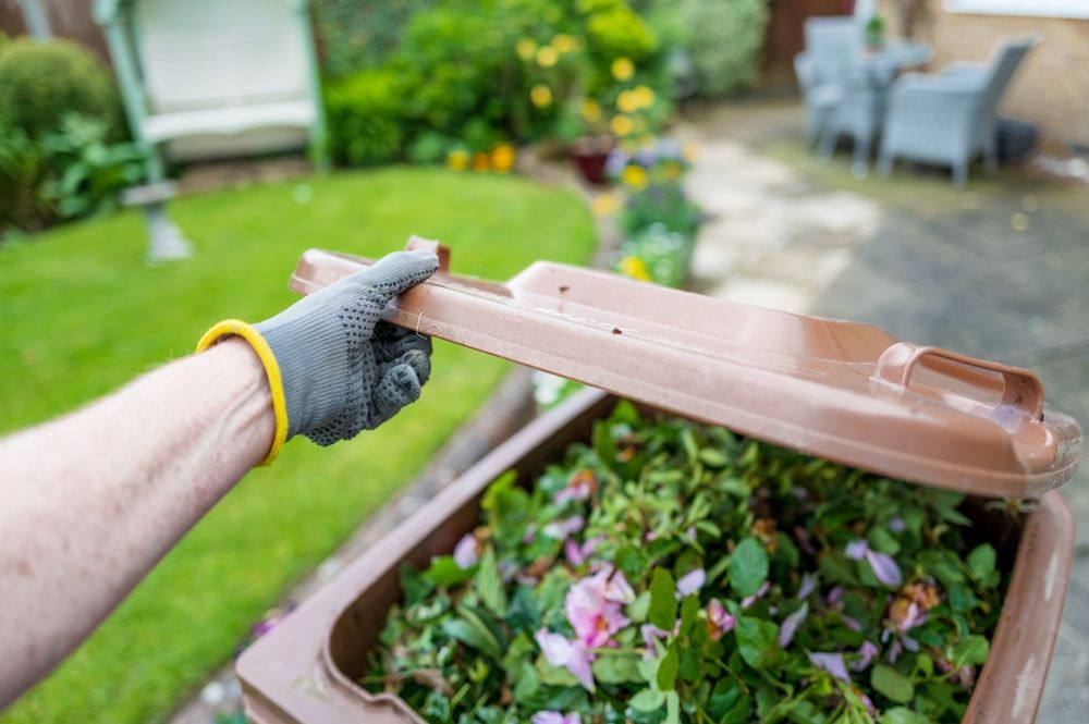 Person in Grey Glove Lifts Brown Compost Bin Lid — All Suburbs Garden Bags in Machans Beach, QLD