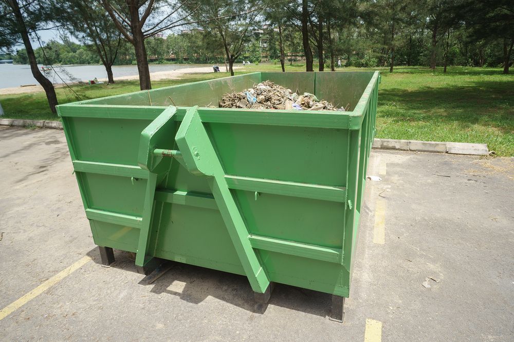 Green Dumpster Filled With Trash on Pavement — All Suburbs Garden Bags in Redlynch, QLD
