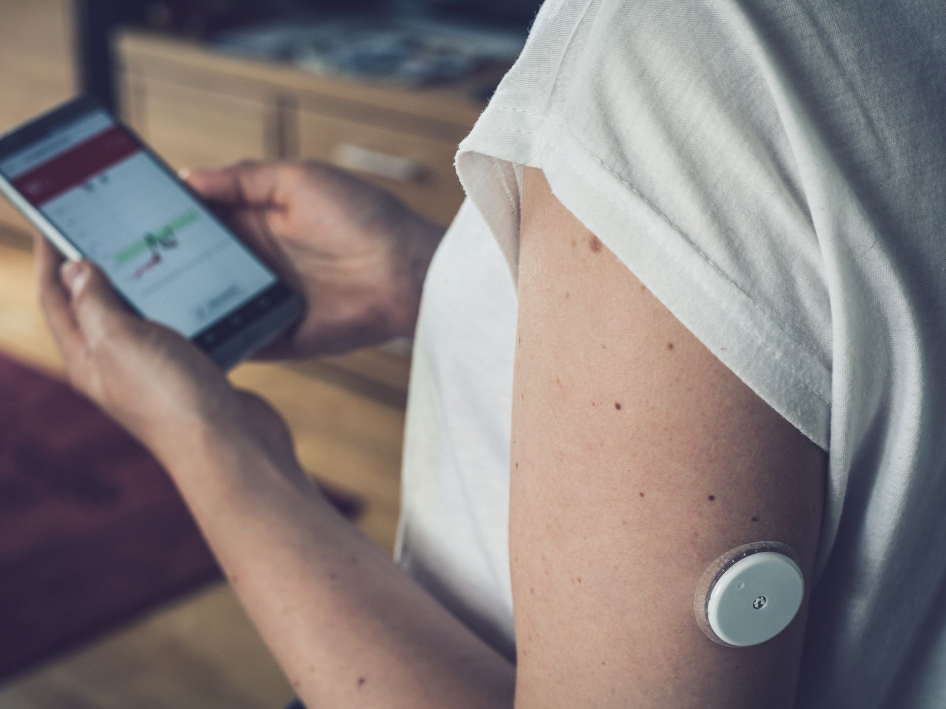 Een persoon draagt ​​een continue glucosemonitor op zijn bovenarm en houdt een smartphone vast waarop een grafiek van de bloedsuikerspiegel te zien is.