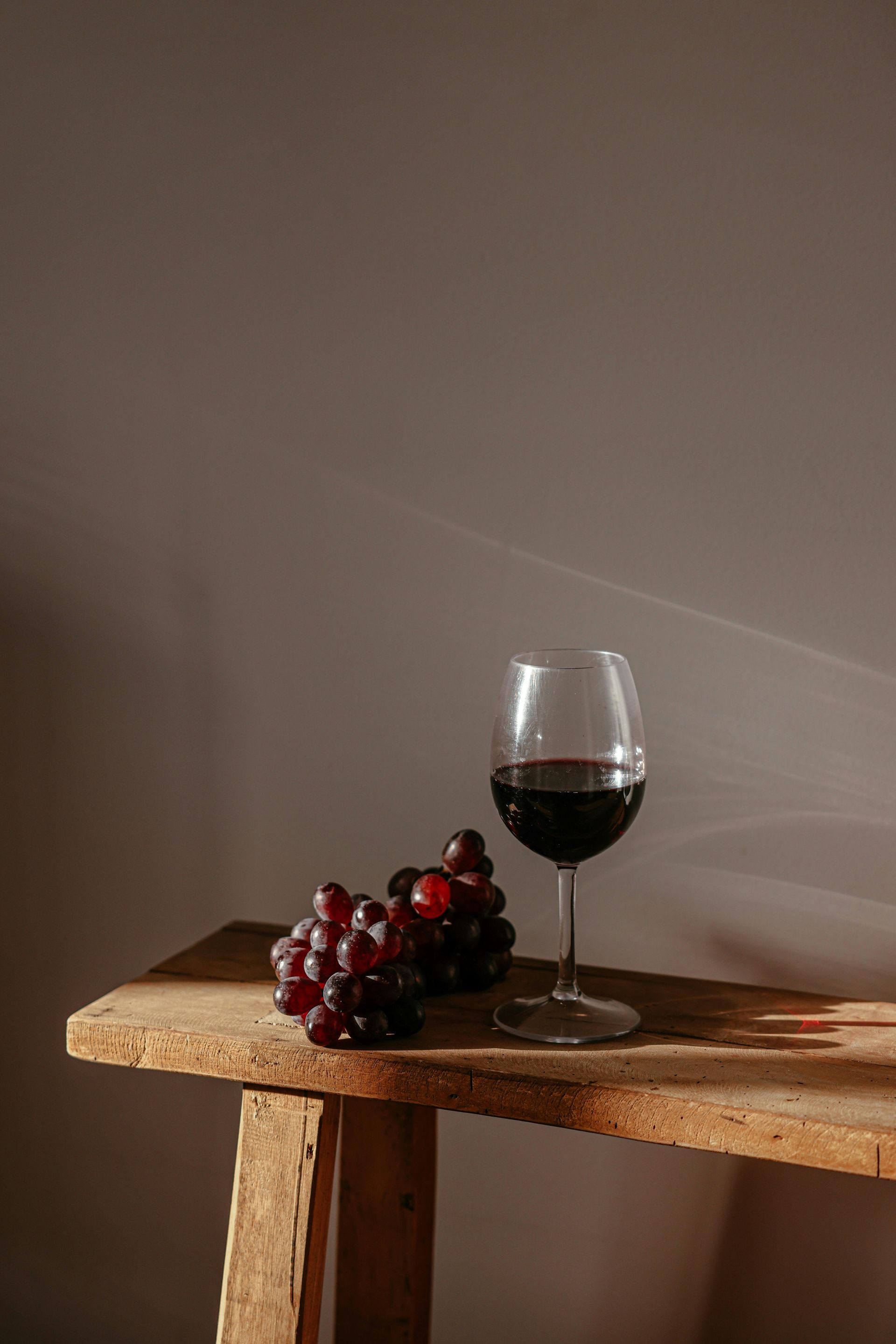 A glass of red wine and a bunch of grapes on a wooden table.