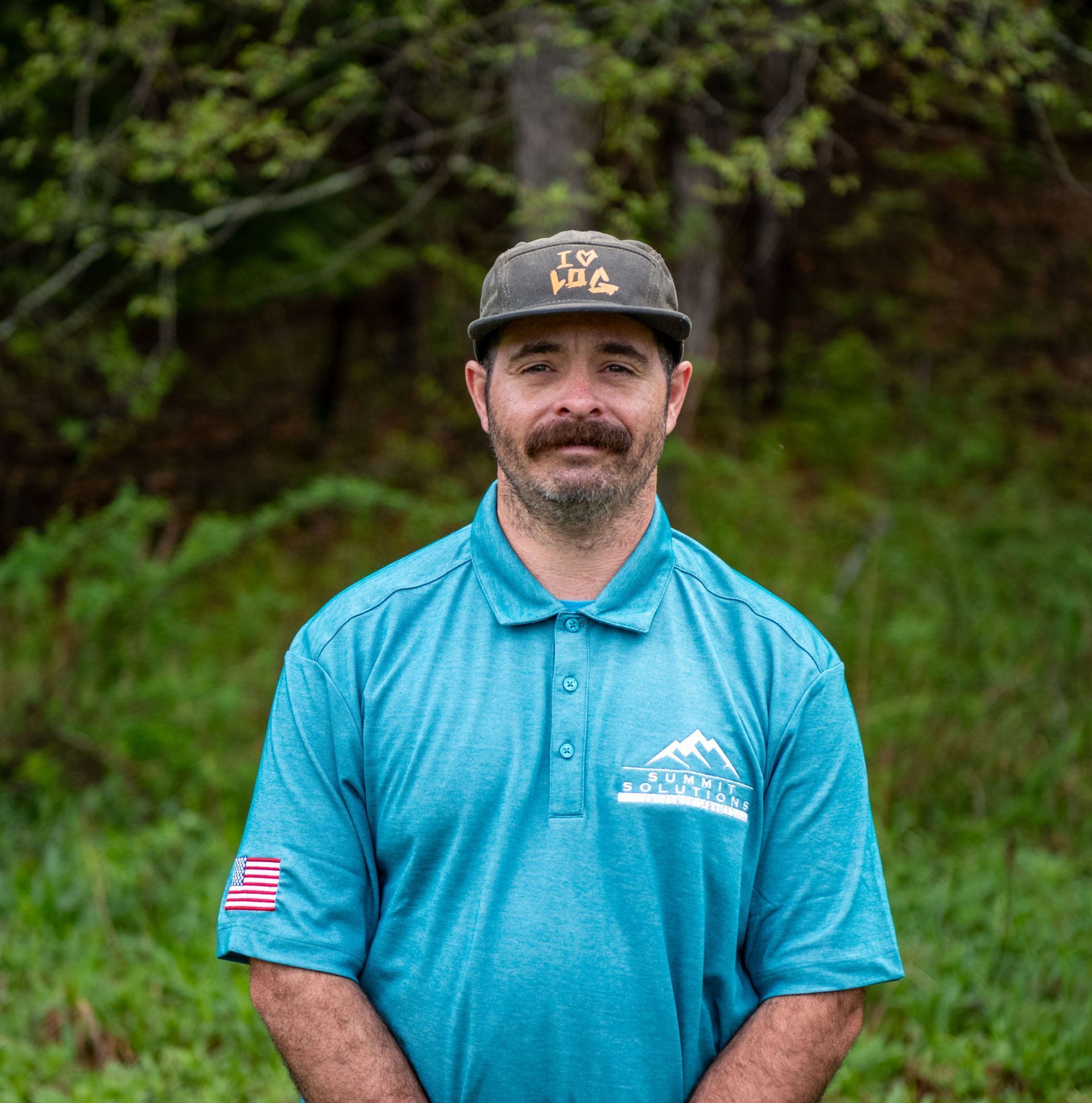 A man wearing a hat and a blue shirt is standing in the grass.
