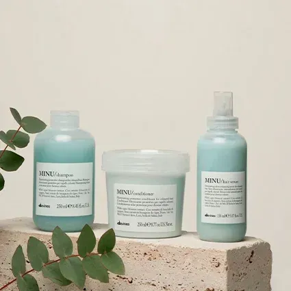 Three blue-tinted hair products on a stone surface: shampoo, conditioner, and hair serum. Eucalyptus branch on the side.