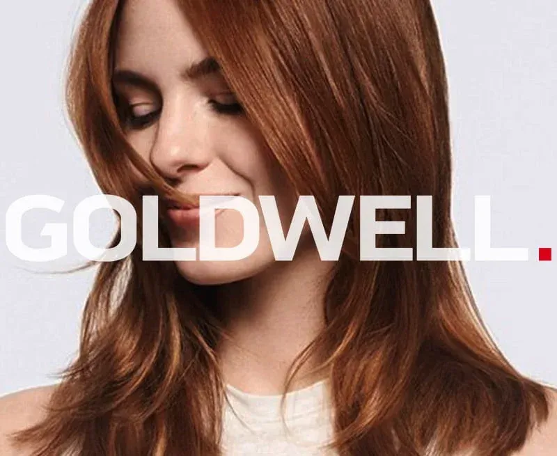 Woman with red hair, eyes closed, smiling, in a Goldwell advertisement.