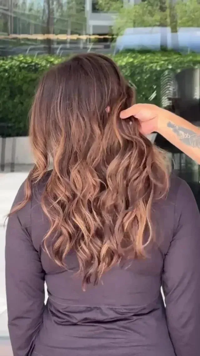 Brown wavy hair, styled. Hand touches hair outdoors.