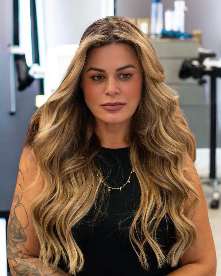Woman with long, wavy blonde hair wearing a black top and gold necklace.