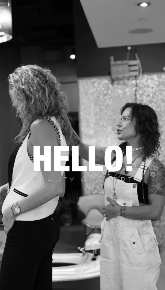 Two women in a salon; one in overalls, the other in a tank top. 