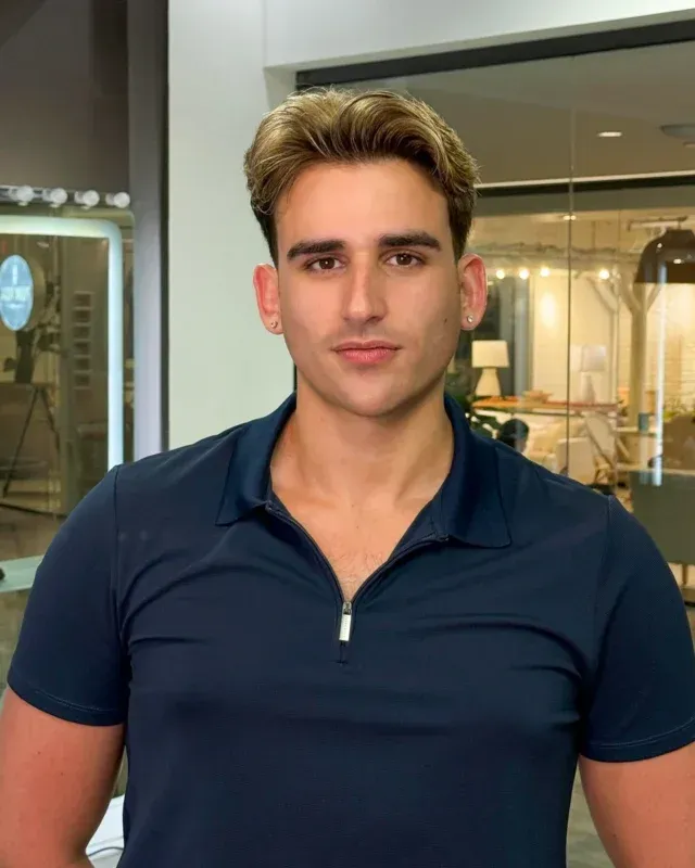 Man with light brown hair, wearing a dark blue polo shirt, standing indoors with a neutral expression.