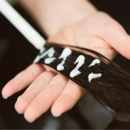 Hand holding a strand of dark hair with applied white hair product.