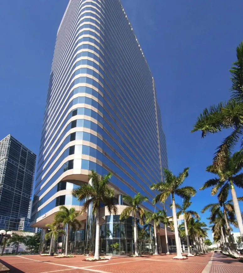 Tall modern skyscraper with reflective blue glass facade, palm trees, and clear blue sky.