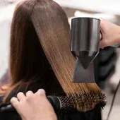 Hairdresser using a hair dryer and round brush to style brown hair in a salon.