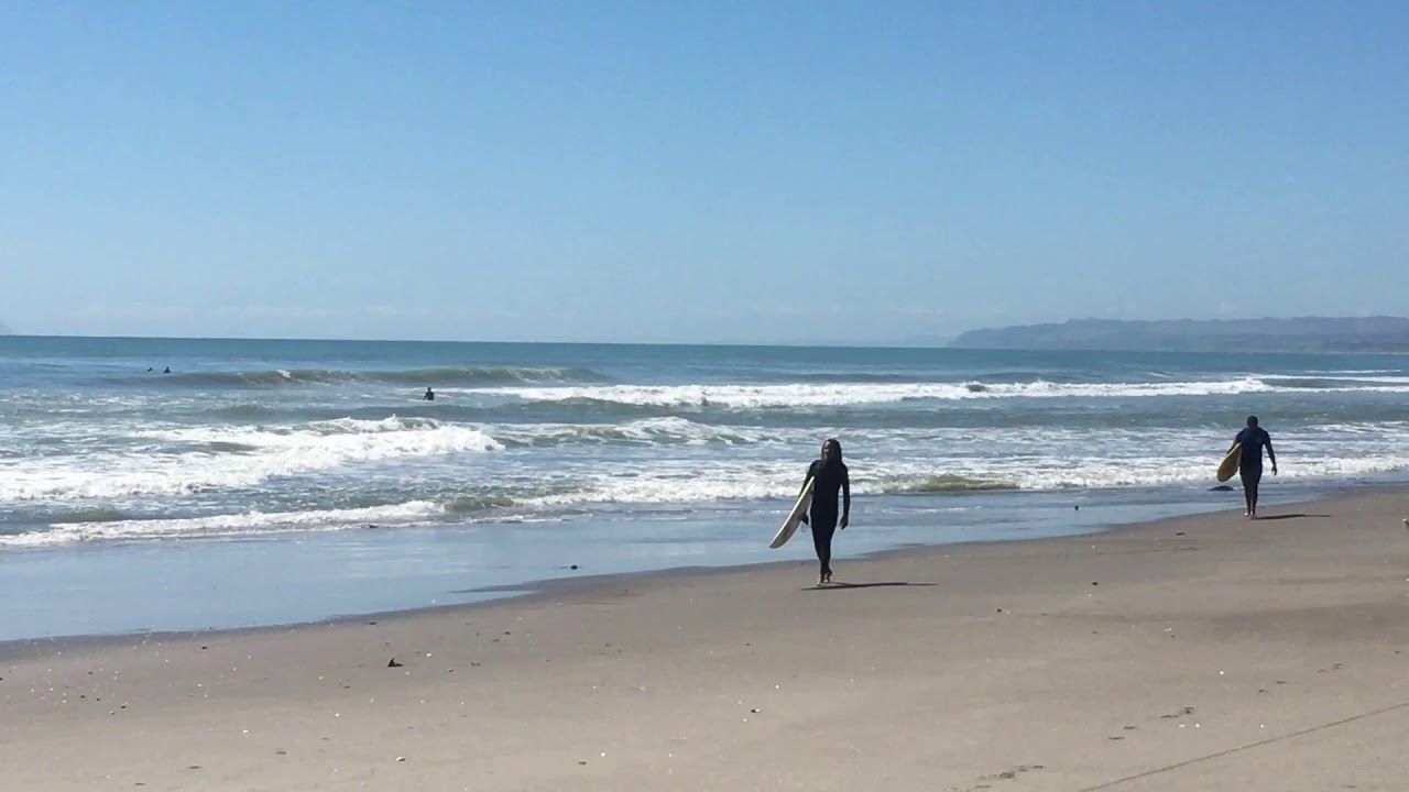 Two people are walking on a beach carrying surfboards.