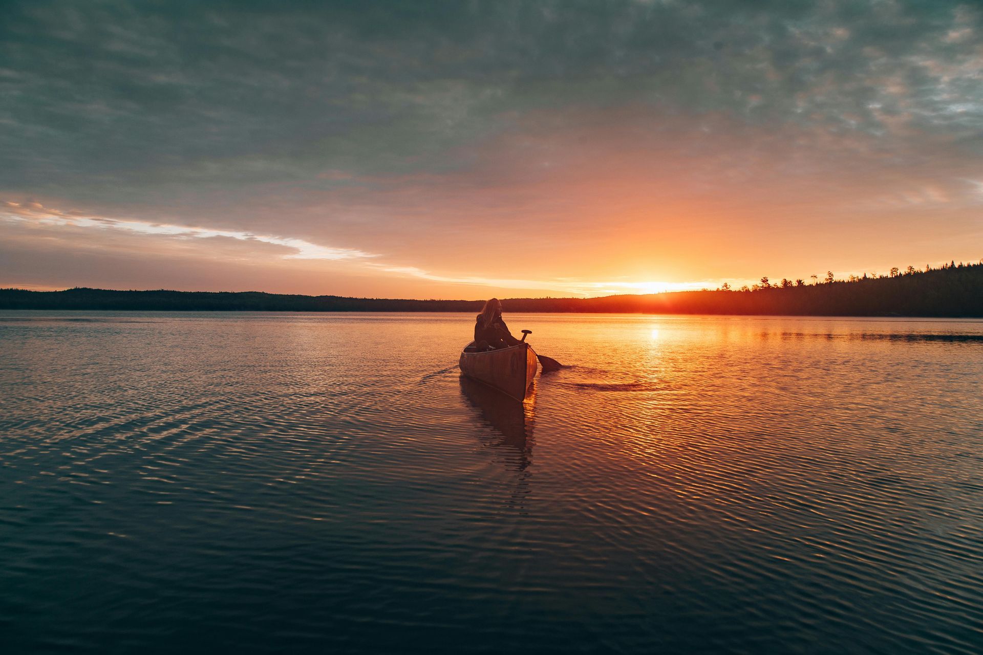 A person is paddling a canoe on a lake at sunset.