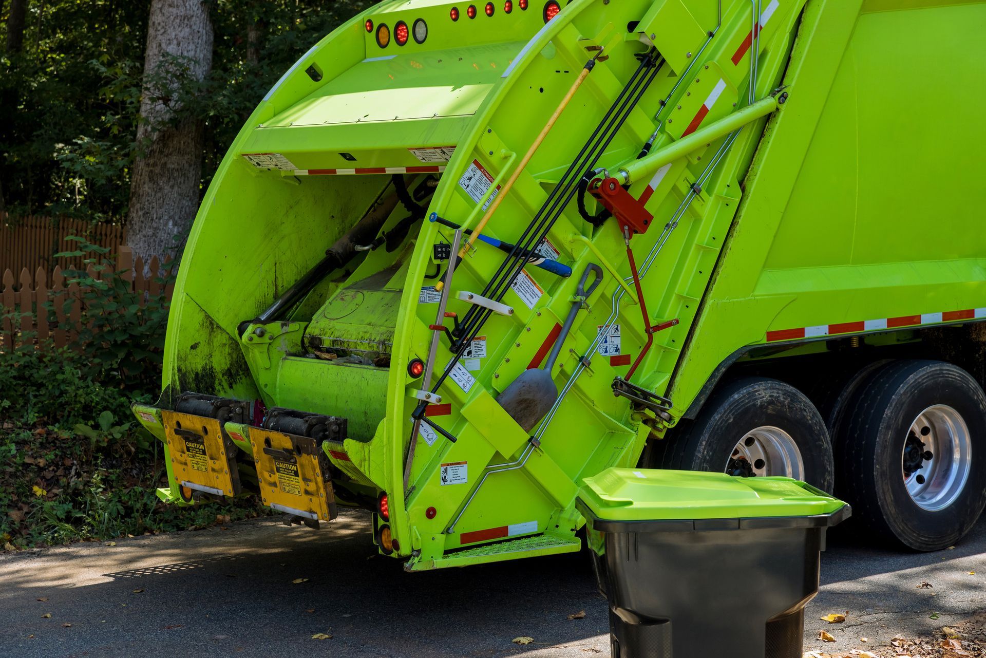 A green garbage truck is in a residential area, next to a garbage unit of the same color. A green garbage truck is in a residential area, next to a garbage unit of the same color.