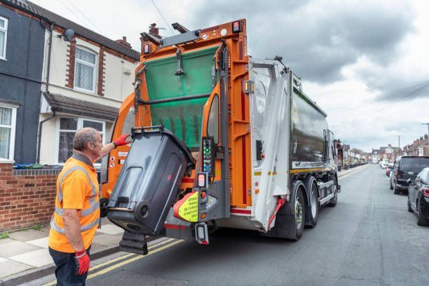 A male garbage pickup worker in the street next to a truck.