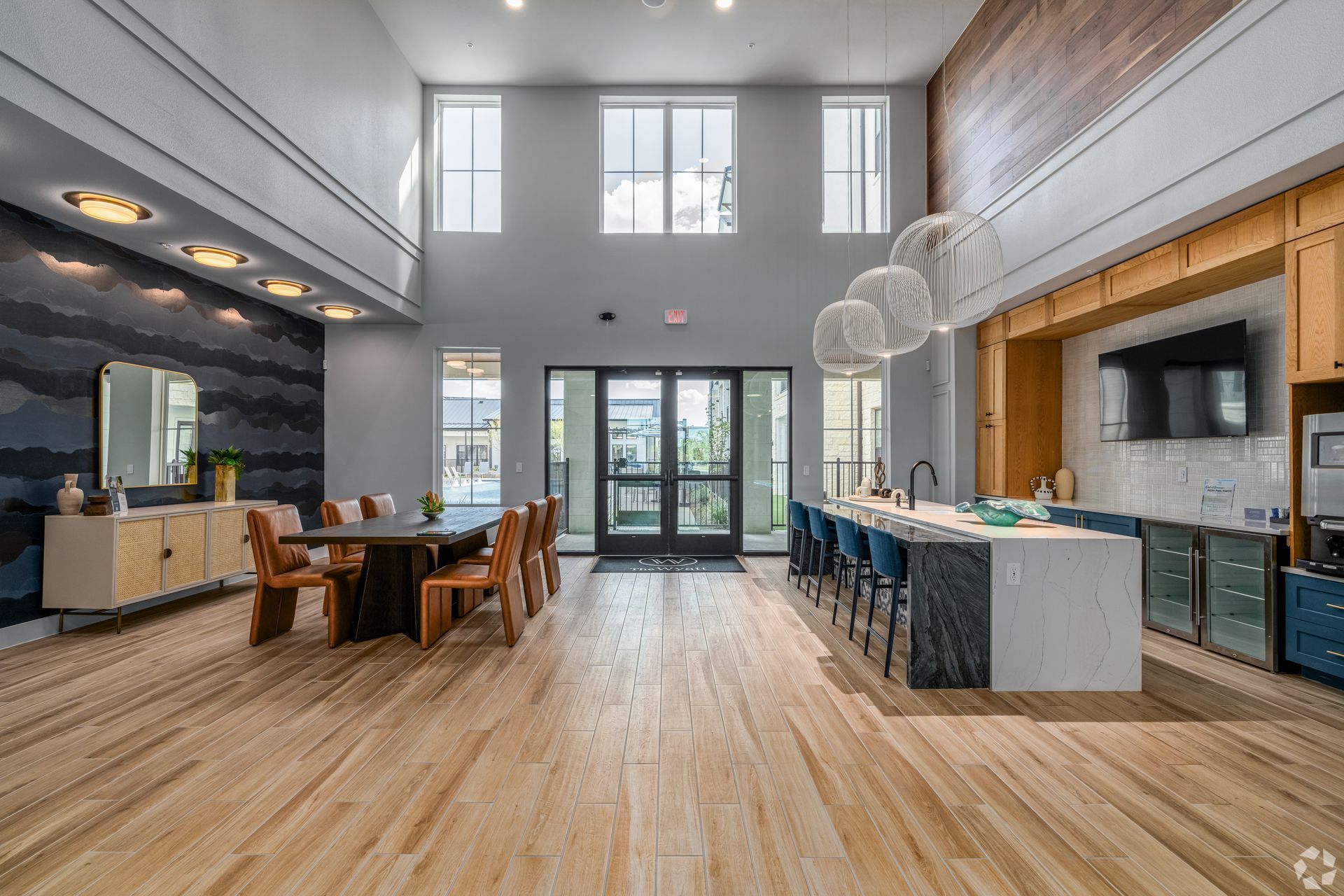 High-ceiling clubhouse with a table, chairs, windows, kitchen, and seating area in it at The Wyatt, offers luxury apartments in North Austin, TX.