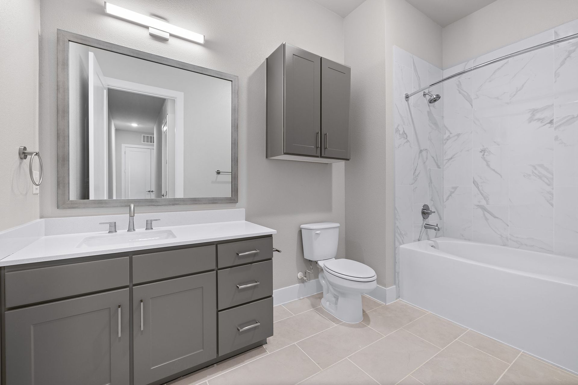 A modern bathroom with a toilet, sink, grey cabinets, mirror, and bathtub at The Wyatt, offers luxury apartments for rent in Austin, TX.