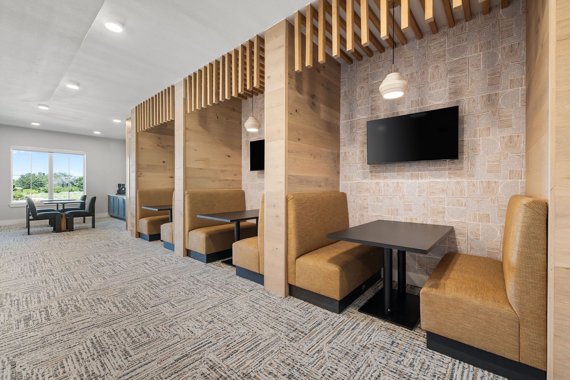 Business center with private work pods, tables, and chairs and a television on the wall at The Wyatt, offers luxury apartments in North Austin, TX.