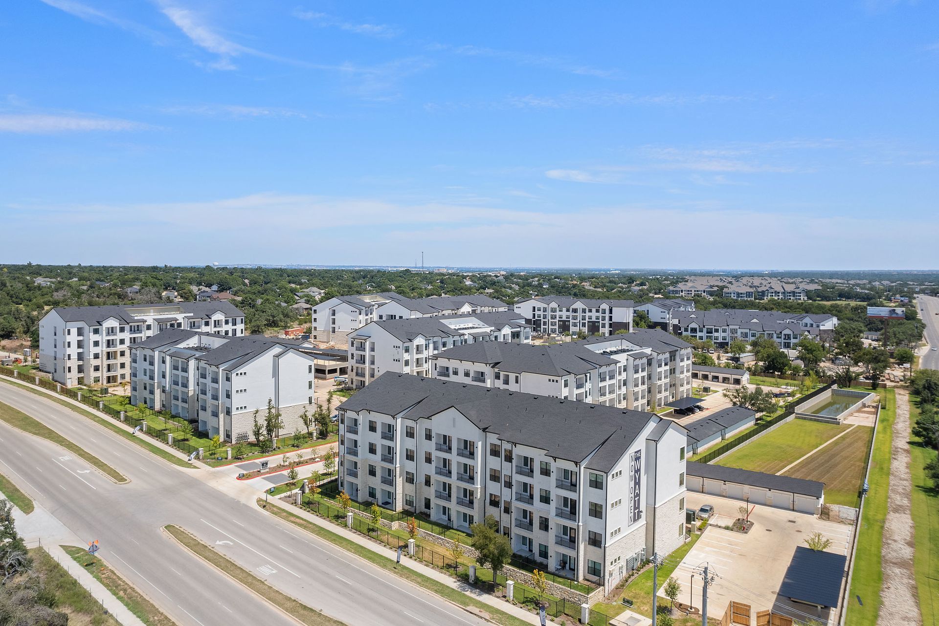 An aerial view of a large apartment complex surrounded by trees and a road at The Wyatt, offers luxury apartments in Austin, TX.