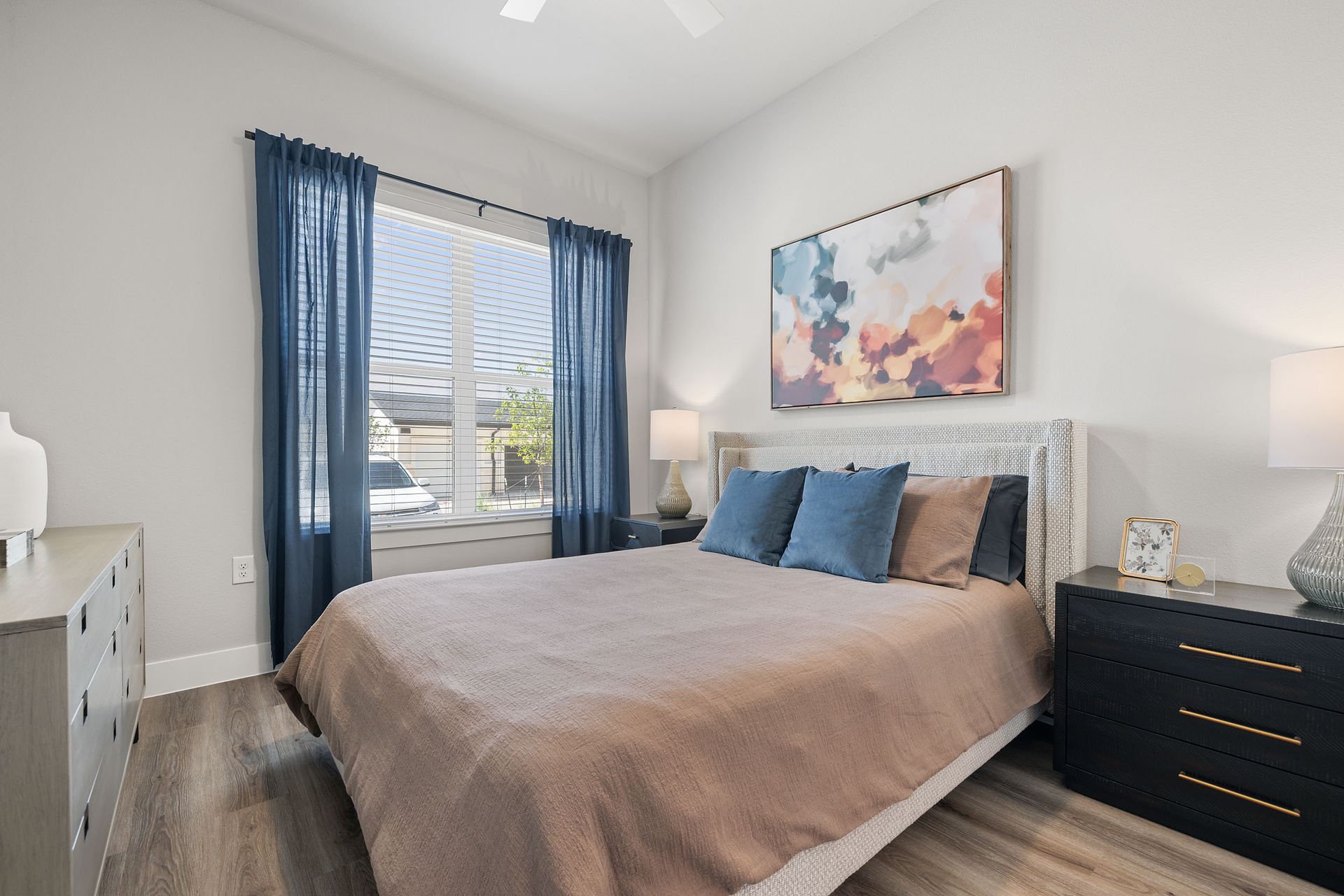 A bedroom with a large bed, dresser, nightstand, and window at The Wyatt, offers luxury apartments in North Austin, TX.
