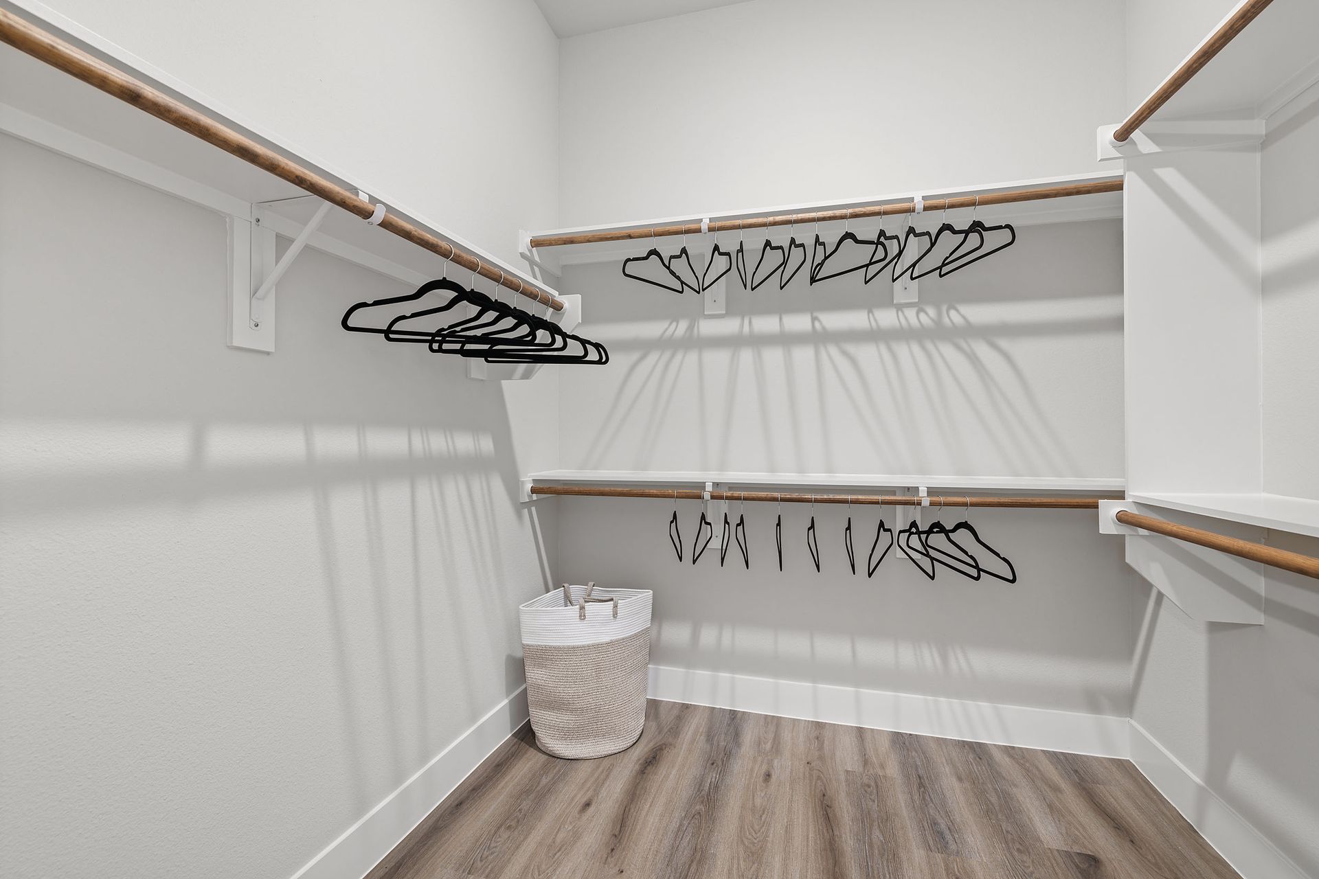A walk-in closet with clothes hanging on the shelves and a laundry basket at The Wyatt offers luxury apartments in North Austin, TX.