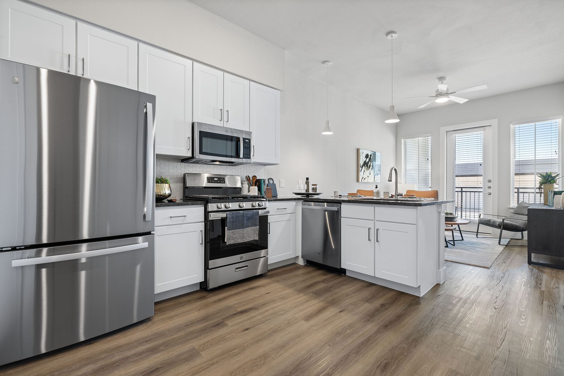 A kitchen with stainless steel appliances and white cabinets oversees the apartment living room and balcony at The Wyatt, offers luxury apartments in North Austin, TX.