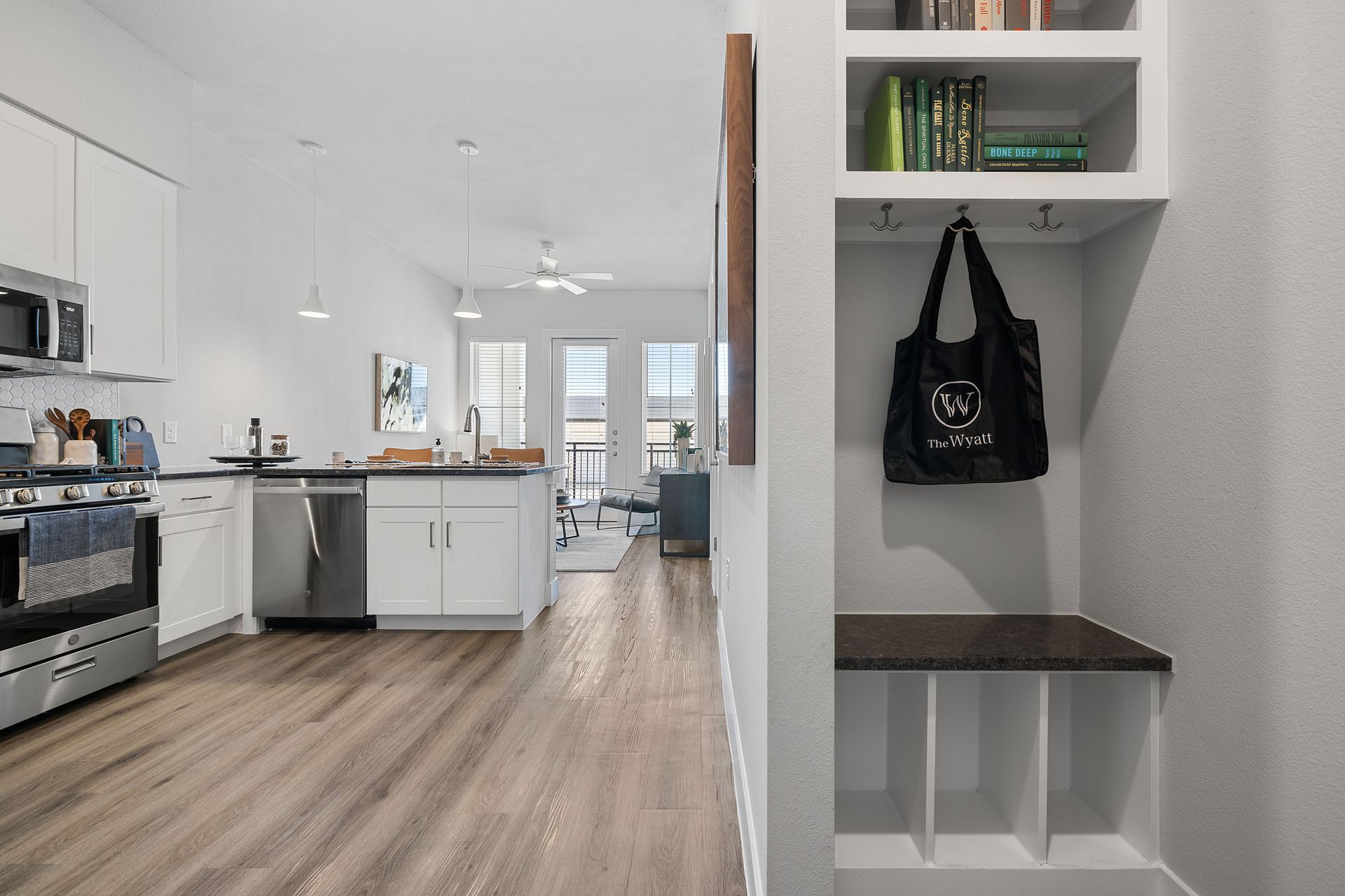 A view from the apartment entrance with a kitchen, hardwood floors, living room, balcony, and a bag hanging on the wall with space for hangers at The Wyatt, offers luxury apartments in North Austin, TX..