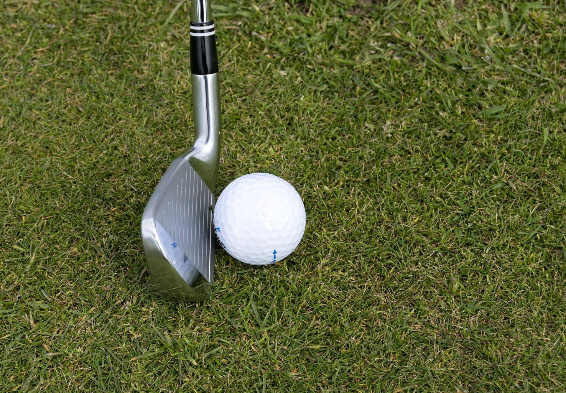 A golf club head positioned next to a white golf ball on a lush green grass fairway.