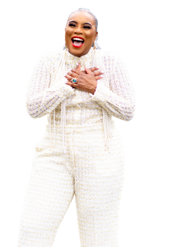 A woman in a white jumpsuit is laughing with her hands on her chest.