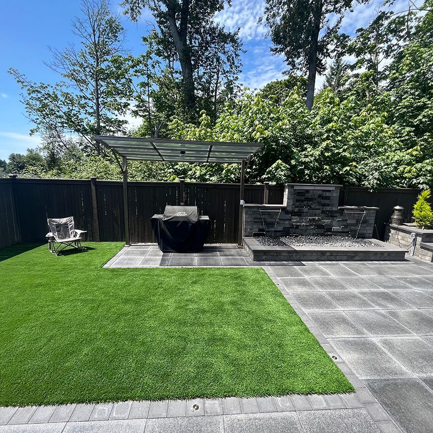 A patio with a grill and chairs in a backyard.