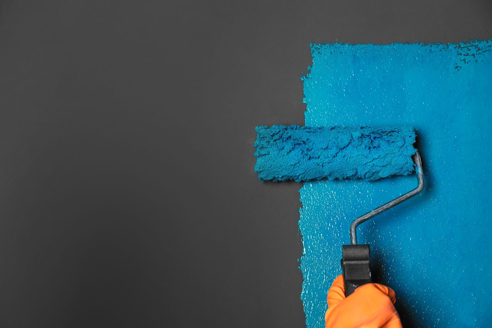 A person is painting a wall with a blue paint roller.