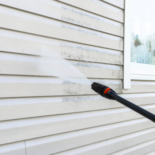 A person is using a high pressure washer to clean the side of a house.