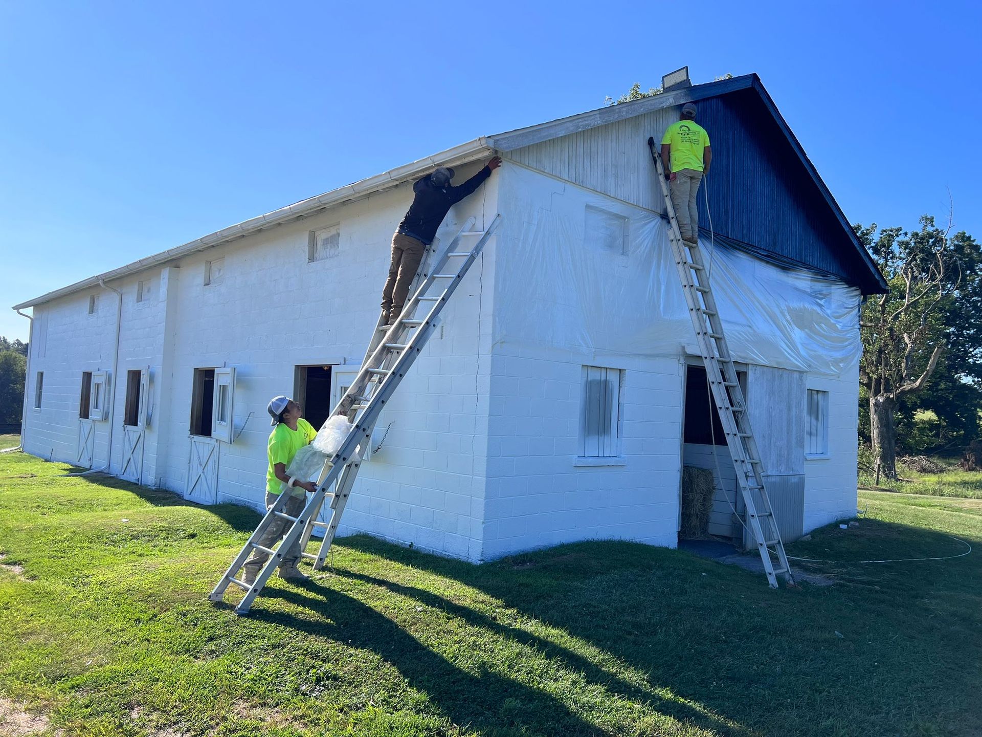 Two men are painting a white barn with ladders.