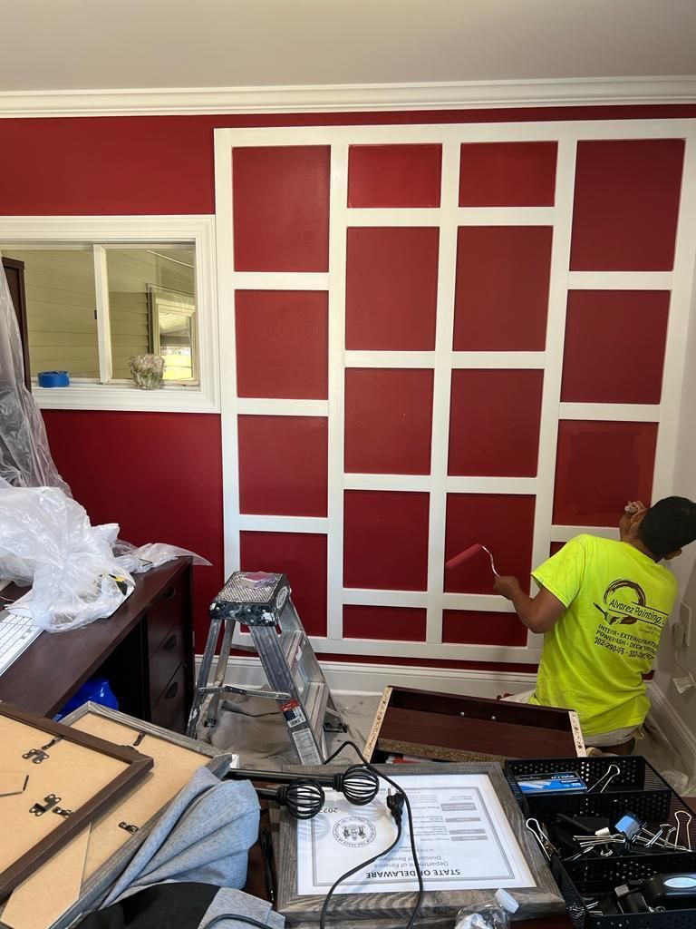 A man is painting a red wall with white squares.